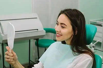 woman smiling in the mirror after her cosmetic dentistry appointment at Clayton Dental Group