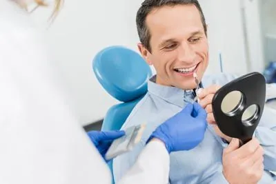 patient color-matching his teeth and dental veneers in the mirror at Clayton Dental Group